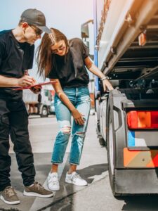 Two professional truck drivers stand in front of the big truck. They talk and perform a technical inspection of the vehicle before next drive. Professional transportation concept.